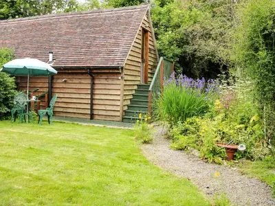 a garden with a cabin with a table and an umbrella at Milford Tree Tops in Craven Arms