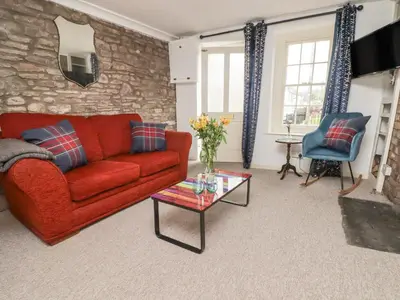 a living room with a red couch and a stone wall at Kooky Cottage in Brecon