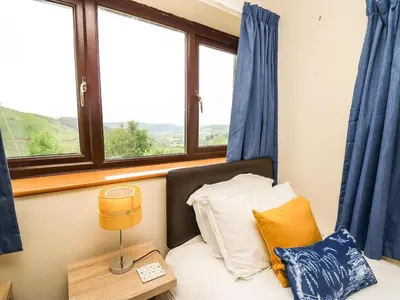 a bedroom with a bed with blue curtains and a window at Pant Y Rhedyn in Llandrindod Wells