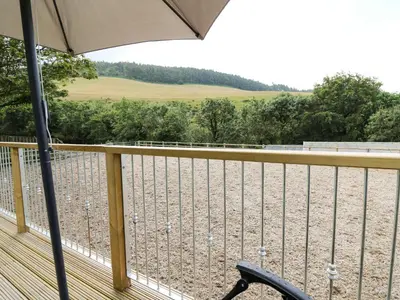 a deck with a chair and an umbrella at Caban Glas in Aberystwyth