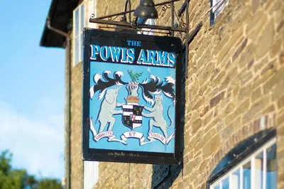 a sign for thepes arms hanging on a brick building at The Powis Arms in North Lydbury