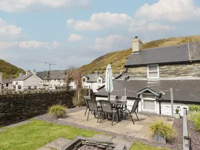 a patio with a table and chairs in front of a house at Arthurs Cottage in Tywyn