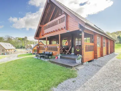 a wooden house with a porch and a lawn at Sun View Lodge in Llanbedr
