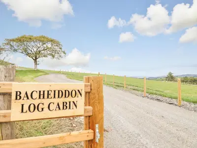 a wooden sign on a fence on a dirt road at Bacheiddon Log Cabin in Machynlleth