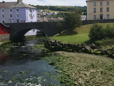 a bridge over a river with buildings in the background at The Granary in Llanddeiniol