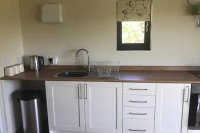 a kitchen with white cabinets and a sink and a window at Secluded Log Cabin in beautiful private gardens in Broxwood