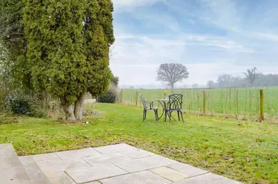 two chairs and a table in a field with a tree at Secluded Log Cabin in beautiful private gardens in Broxwood