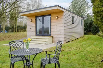 a small cabin with a table and chairs in front of it at Secluded Log Cabin in beautiful private gardens in Broxwood
