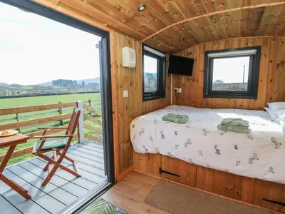 a bedroom in a wooden cabin with a bed and a balcony at Claerwen in Llandrindod Wells