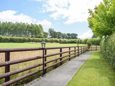 a wooden fence with a sidewalk next to a field at The Lodge At Forbury Cottage in Kimbolton