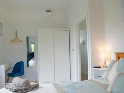 a white bedroom with a bed and a blue chair at The Lodge At Forbury Cottage in Kimbolton