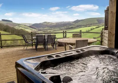 a hot tub on a deck with a table and chairs at Beacons View Farm Cottages in Merthyr Cynog