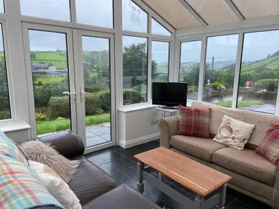 a living room with a couch and a tv and windows at 4 bedroom bungalow in peaceful countryside with log burner - Talar Deg, Capel Madog in Capel Madog