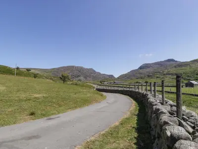 a road next to a stone fence on a hill at Llethr - Shepherds Hut in Llanbedr