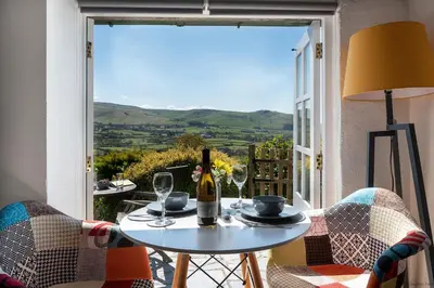 a table with a bottle of wine and glasses on a balcony at Cozy Log Burner Cottage & On-Site Dog Field in Bryn-crug