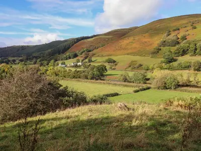 a grassy hillside with a farm in the distance at 1 Hendom in Corwen