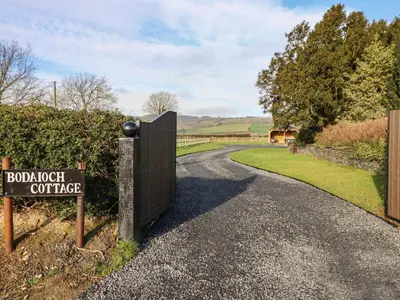 a gate with a sign on a road with a fence at Bodaioch Cottage in Caersws
