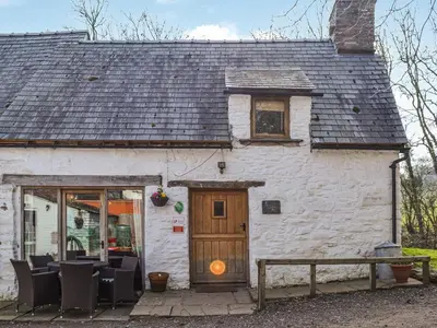 a white building with a wooden door and chairs at Ty Fferm Hen - Uk36420 in Talybont