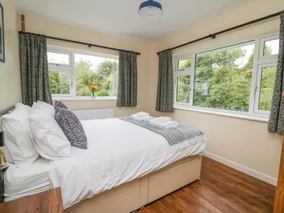 a bedroom with a bed and two windows at Ger Yr Afon Cottage in Rhayader