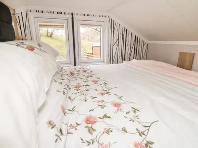 a bedroom with a white bed with pink flowers on it at Meadow Retreat in Rhayader