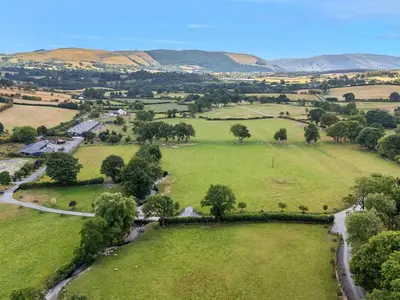 an aerial view of a green field with mountains in the background at Woodland Escape in Rhayader