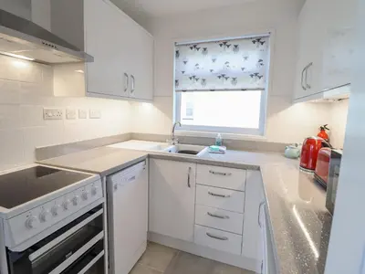 a white kitchen with a sink and a window at 48 Glan Y Mor in Fairbourne