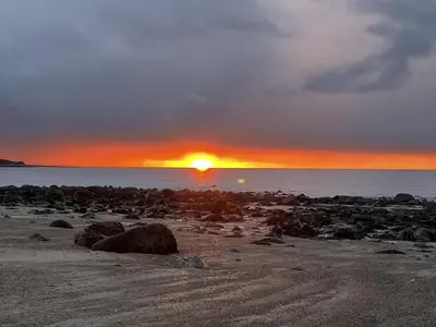 a sunset on a beach with rocks and the ocean at Bwthyn Nain Cottage near Harlech with ocean views in Llanfair
