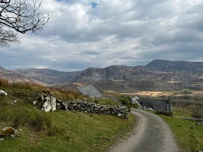 a dirt road in the middle of a field with mountains at Bwthyn Nain Cottage near Harlech with ocean views in Llanfair