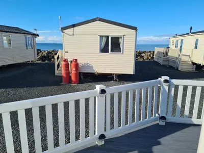 a white fence next to a house and the ocean at Barmouth Lyons Sunnysands 346 in Talybont