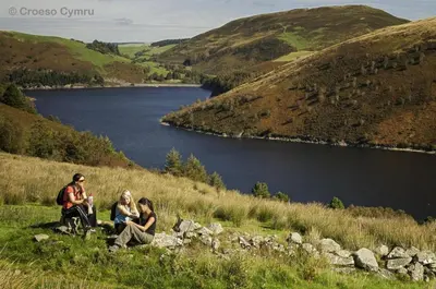 a group of people sitting on a hill overlooking a lake at 2 Bed in Y Drenewydd oc-waa401 in Llanllugan