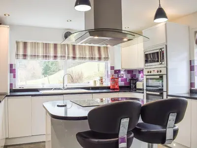 a kitchen with white cabinets and black chairs and a sink at Rhiw Gam in Abbey-Cwmhir