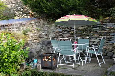a table and chairs under an umbrella next to a stone wall at Homely cottage with garden and mountain-view in Blaenau-Ffestiniog