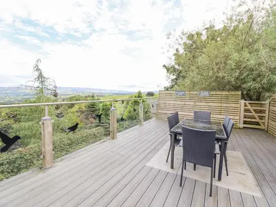 a wooden deck with a table and chairs on it at Hilltop Lodge in Corwen