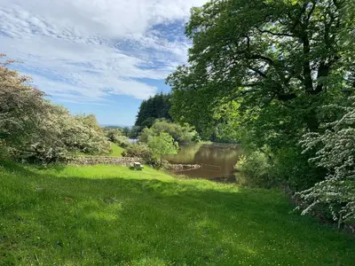 a grassy field with a pond and a river at The Stables at Pentregaer Ucha, tennis court & lake in Oswestry
