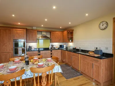 a kitchen with a table with chairs and a clock on the wall at Yr Hen Feudy At Pentre Farm in Llansilin