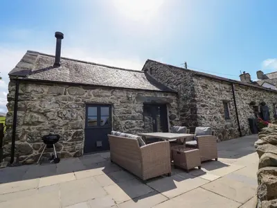 a stone cottage with a table and chairs outside at Beudy Bach in Llanbedr