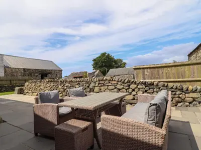 a patio with a table and chairs and a stone wall at Beudy Bach in Llanbedr
