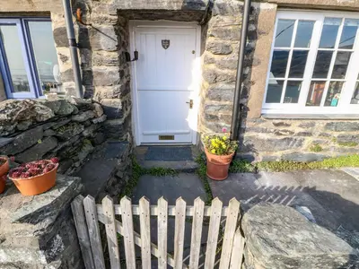 a white door of a stone house with potted plants at 2 Bwth Mawr in Barmouth