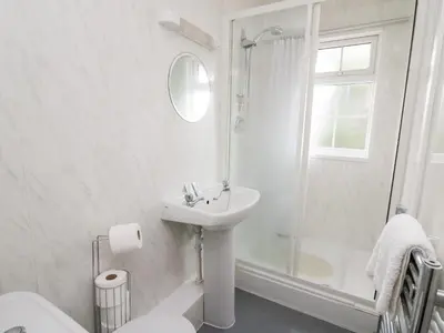 a white bathroom with a sink and a shower at Primrose Cottage in Llandrindod Wells