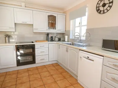 a kitchen with white cabinets and a clock on the wall at Glyn Cottage in Llanon