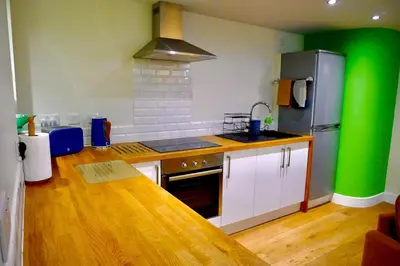a kitchen with white cabinets and a green wall at “Dragons Den” Centrally located Modern Apartment in Aberystwyth