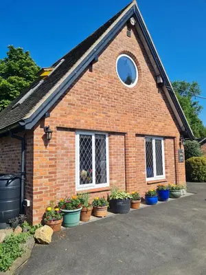 a brick house with potted plants in front of it at Topsy-Turvy, Gardeners Cottage, Clungunford, Ludlow, Shropshire SY70PN in Broome