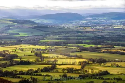 an aerial view of a green field with mountains at Topsy-Turvy, Gardeners Cottage, Clungunford, Ludlow, Shropshire SY70PN in Broome