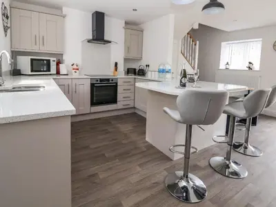 a kitchen with white cabinets and a kitchen island with bar stools at Cae Iocyn in Wrexham