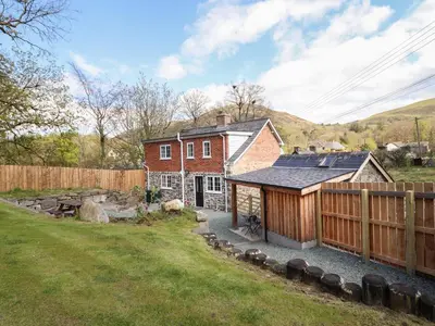 a red brick house with a fence and a yard at Tan Y Capel in Llanbrynmair