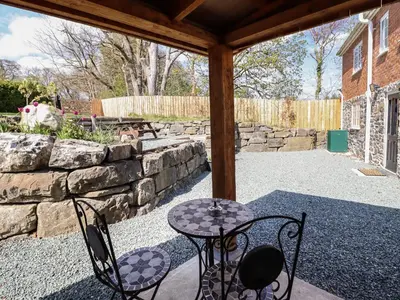 a patio with two chairs and a table and a stone wall at Tan Y Capel in Llanbrynmair