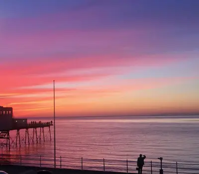 a person standing on a pier at sunset at Seaside Apartment in Aberystwyth