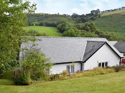 a white house with a gray roof and a green field at Wrens Nest in Llanfair Caereinion