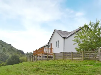 a white house on a hill with a wooden fence at Swallow Cottage in Llanfair Caereinion