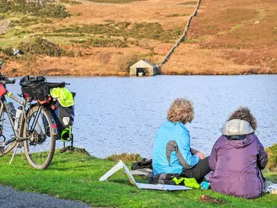two people sitting on the grass near a lake at Gors Y Gader in Llanelltyd
